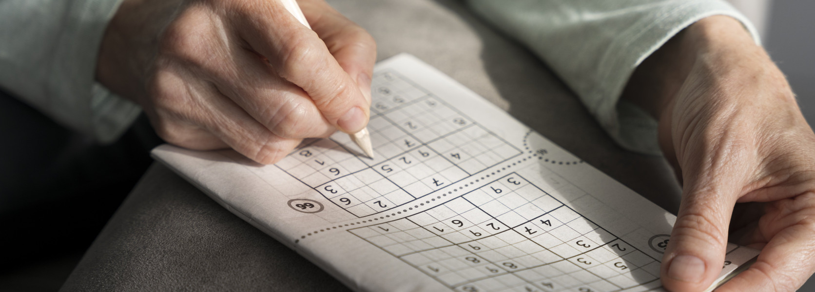 Elderly hands solving a sudoku puzzle with a pencil, staying mentally sharp after retirement