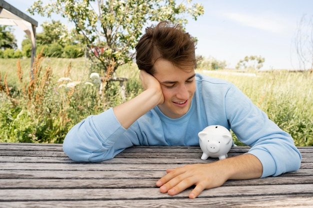 Young man looking at a piggy bank outdoors, mentally shifting from saving mode to spending in retirement